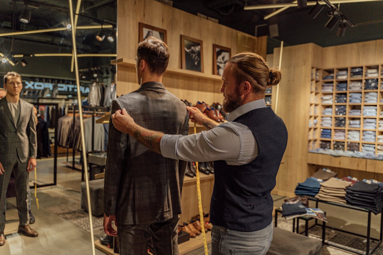 Tailor measuring a client for a suit in a stylish clothing store environment.