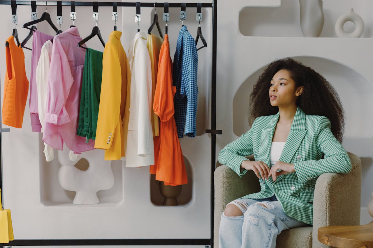 about-01 Stylish woman in green blazer sitting by colorful clothes in boutique.